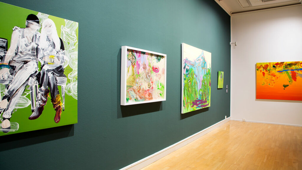 Vihreällä seinällä värikkäitä maalauksia.