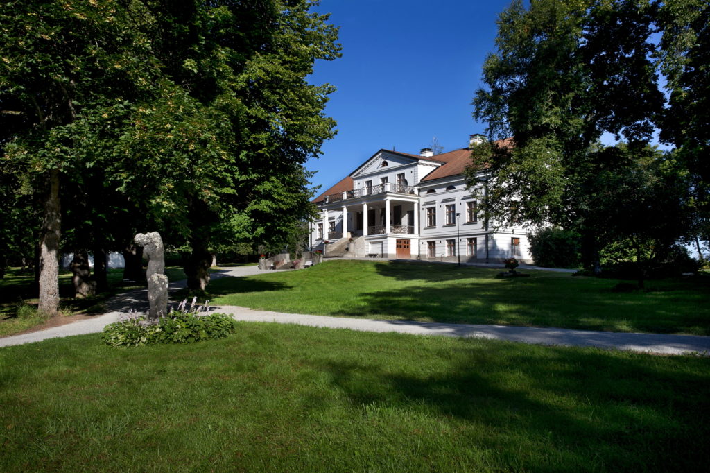 Valkoinen kartanorakennus puistomaisemassa.