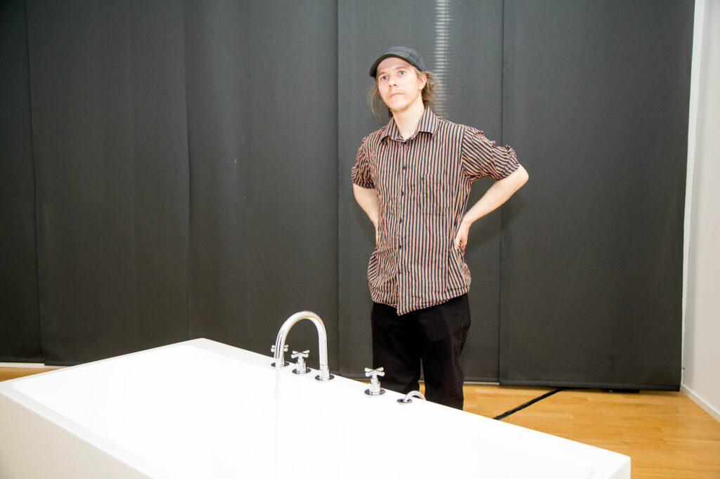 Nuori mies seisoo kylpyammeen takana.
