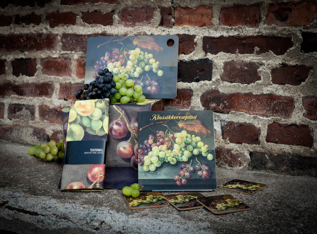 A book, kitchen towel and cutting board with a painting image in front of a brick wall.