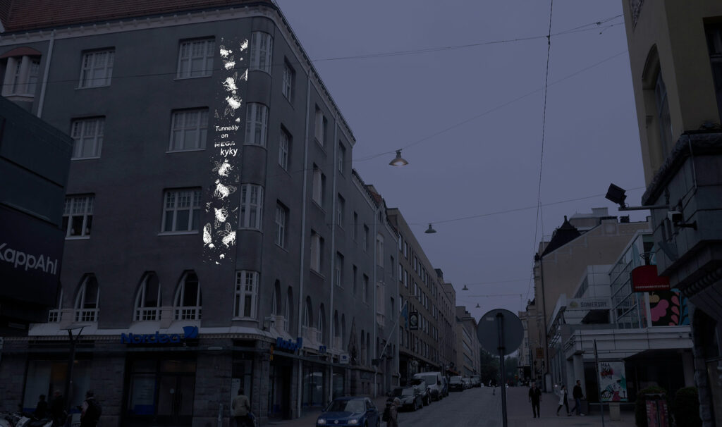 Vanhan kerrostalon seinälle on heijastettu teksstiä ja pieni kuva.