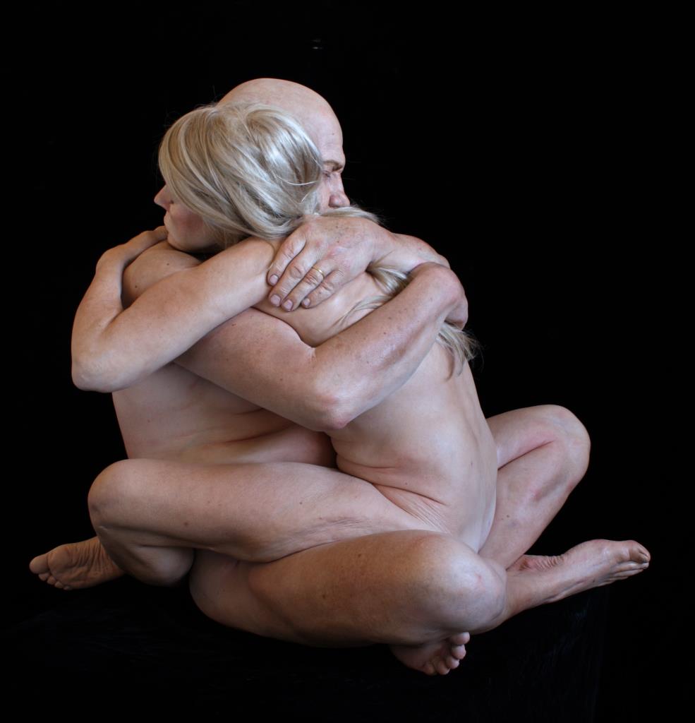 Two naked people sit closedly together hugging each other.
