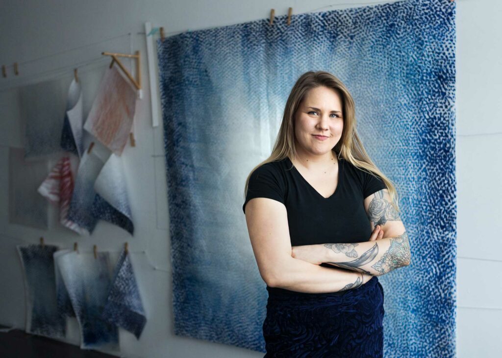 A lady wearing a black dress and standing in front of a large blue work of art.
