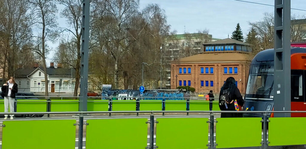 Vihreän aidan takaa näkyy tiilirakennus.