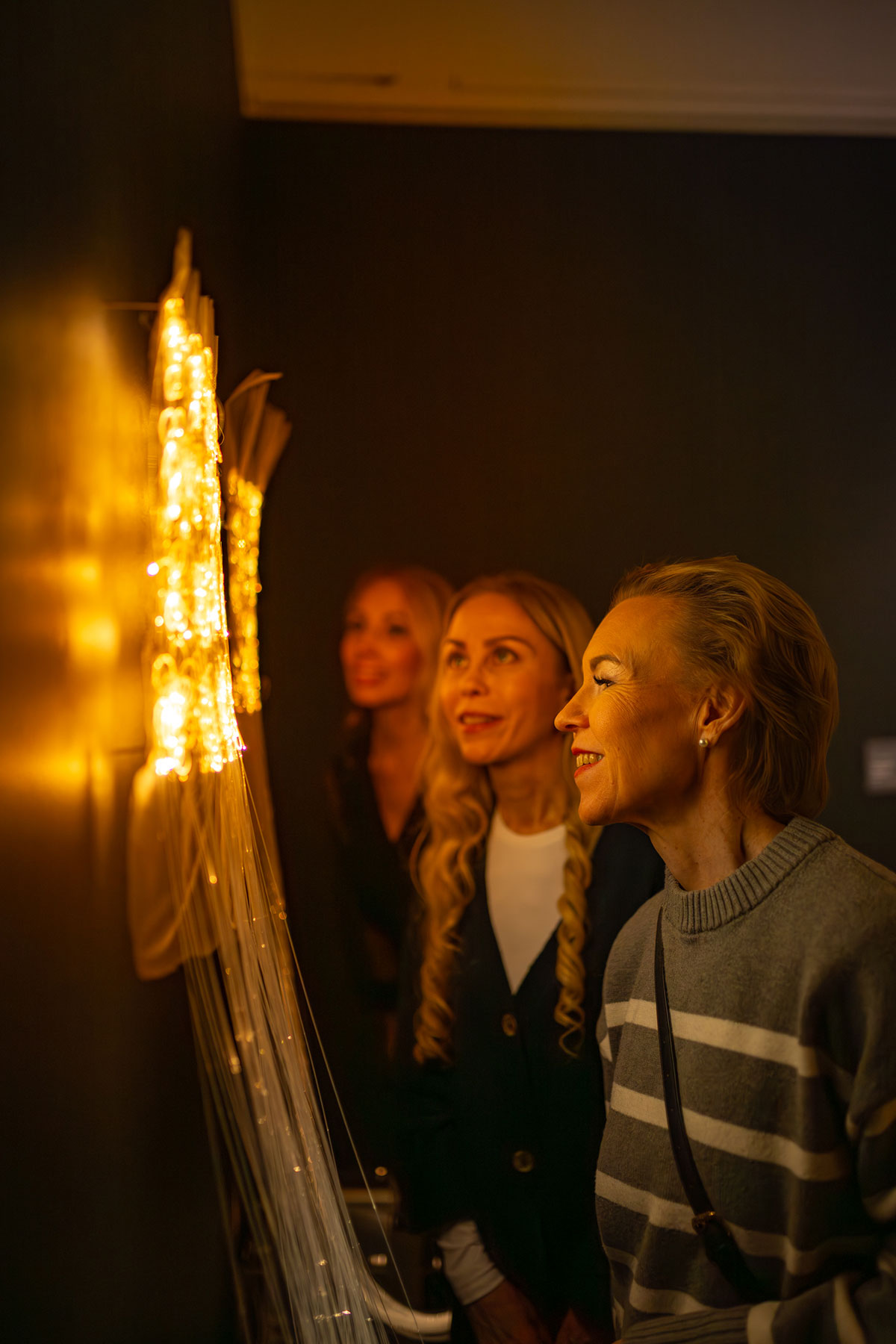 Asiakkaat katsovat valaistua veistosta seinällä.