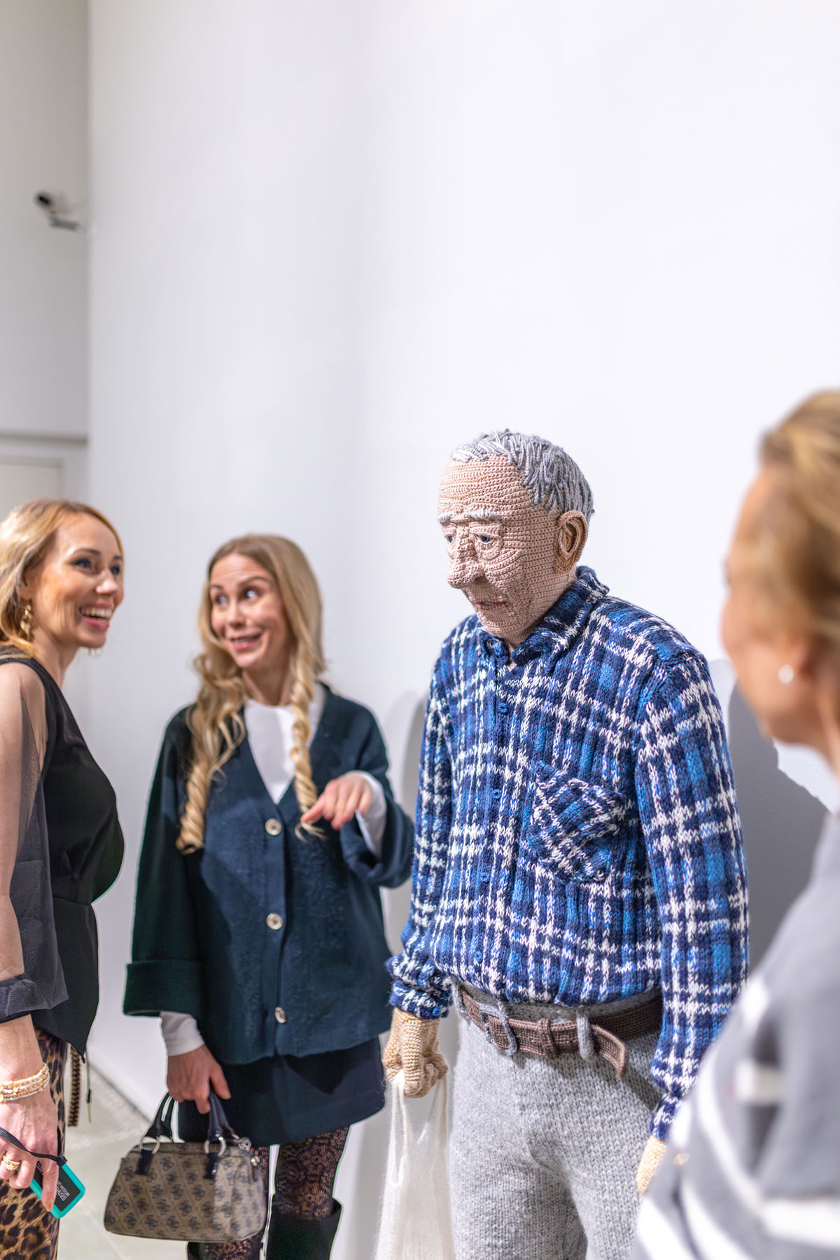 Asiakkaat tutkivat ihmistä esittävää virkattua veistosta.